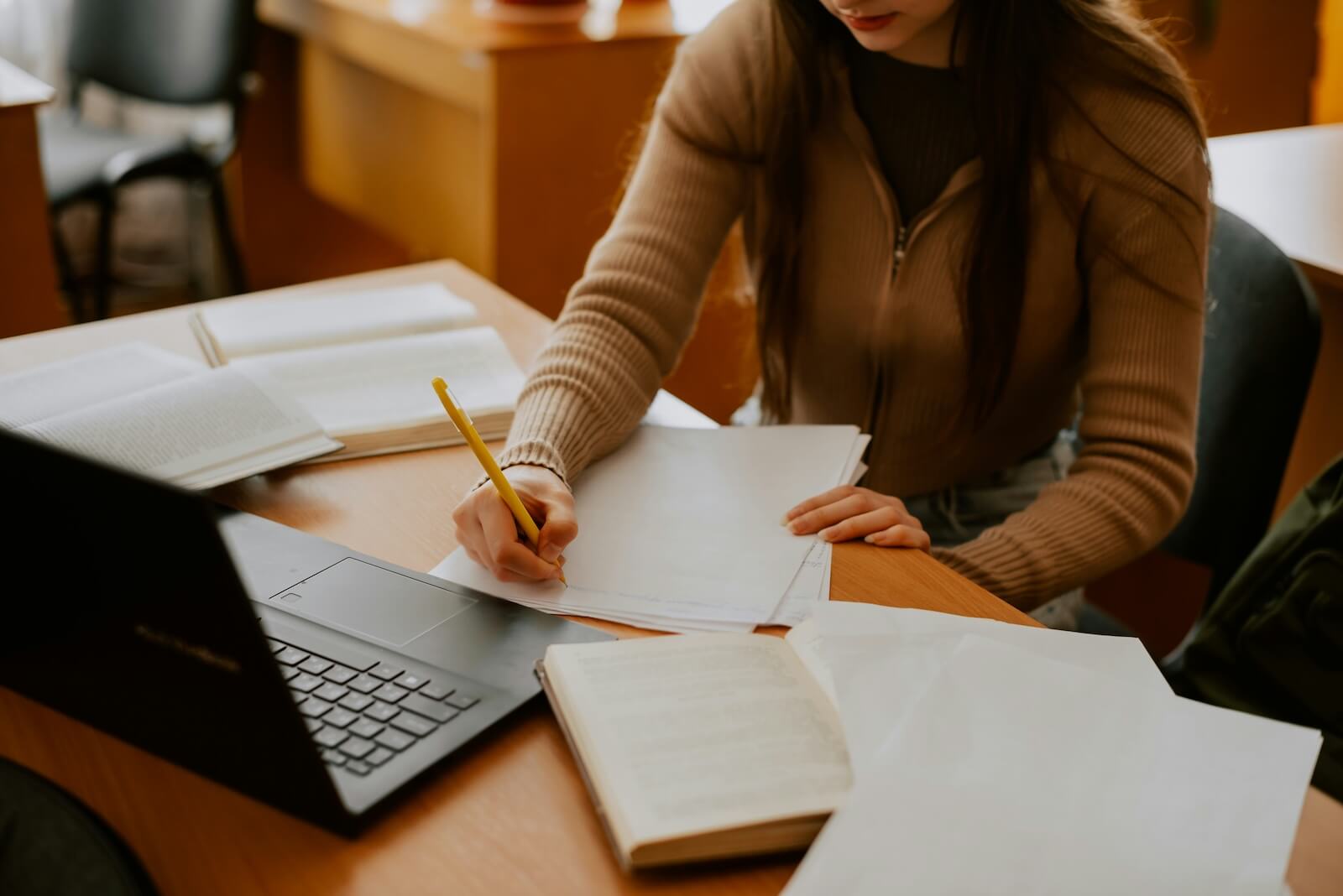 A student with an open laptop and books, writing on papers.