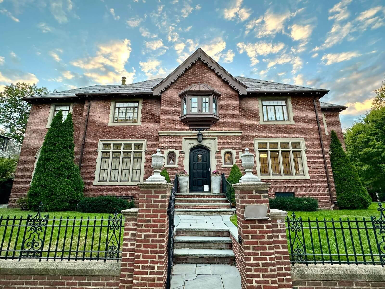 A red brick house with a black front door and stone steps at sunset, like the houses PNMs visit during sorority recruitment.