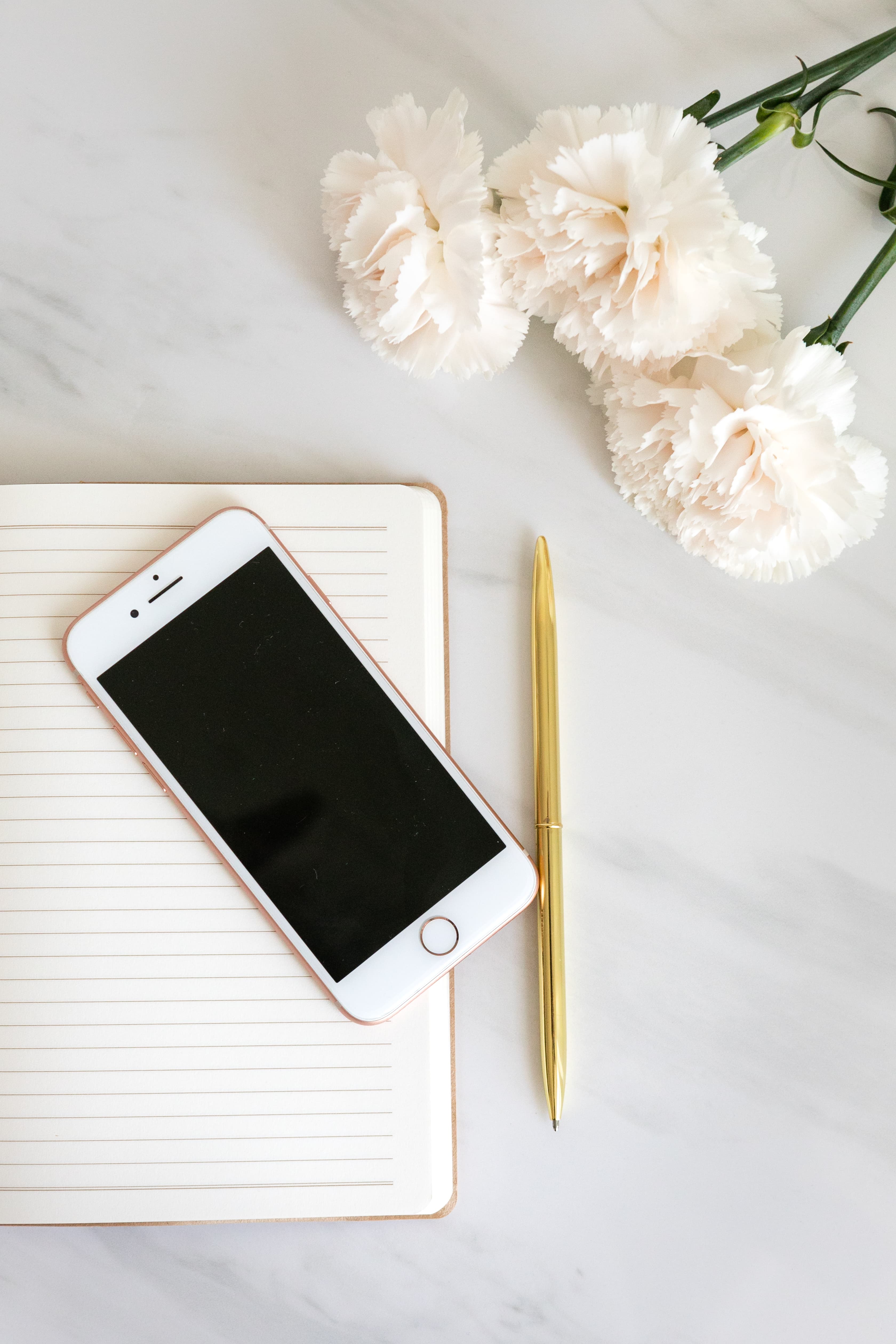 Open planning notebook with a pen, phone, and a soft pink carnation on a light surface