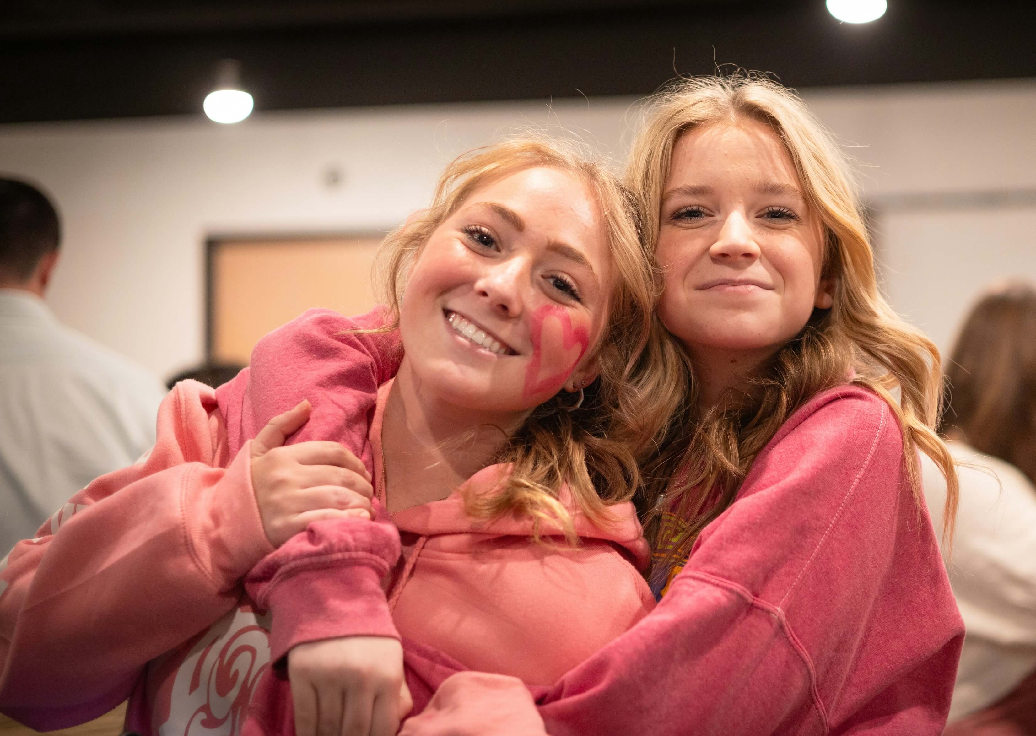 Two college women arms around each other posing for the camera in matching bid day sweatshirts.