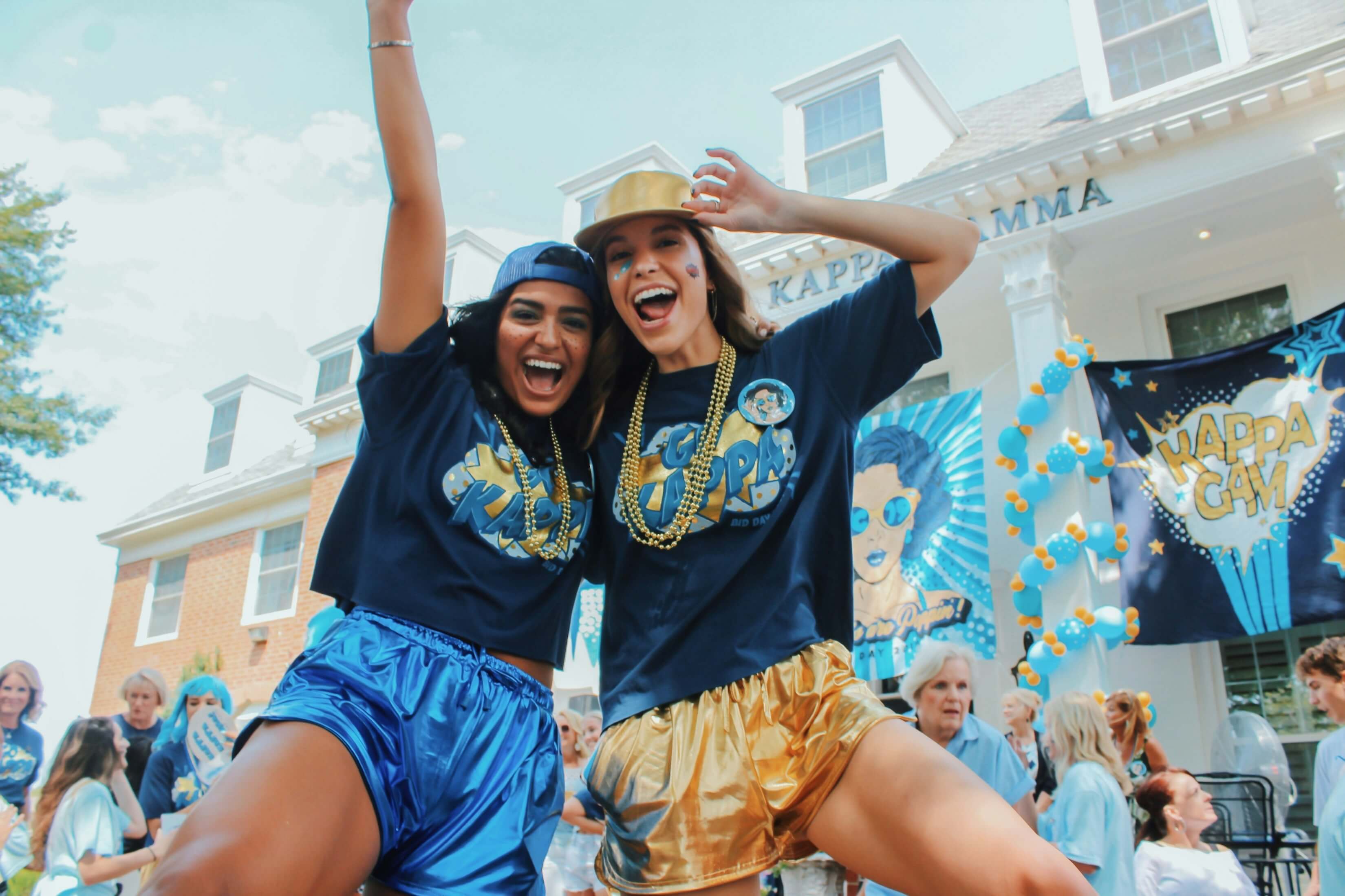 New sorority members in matching bid day shirts hugging outside a chapter house on a sunny morning